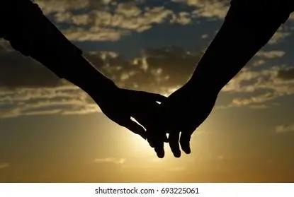 alt=Deux mains qui se rejoignent au coucher du soleil, symbolisant le passage, la connexion et les expériences de mort imminente.